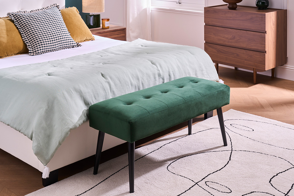 Banc capitonn vert fonc en velours et mtal noir au pied d'un lit.