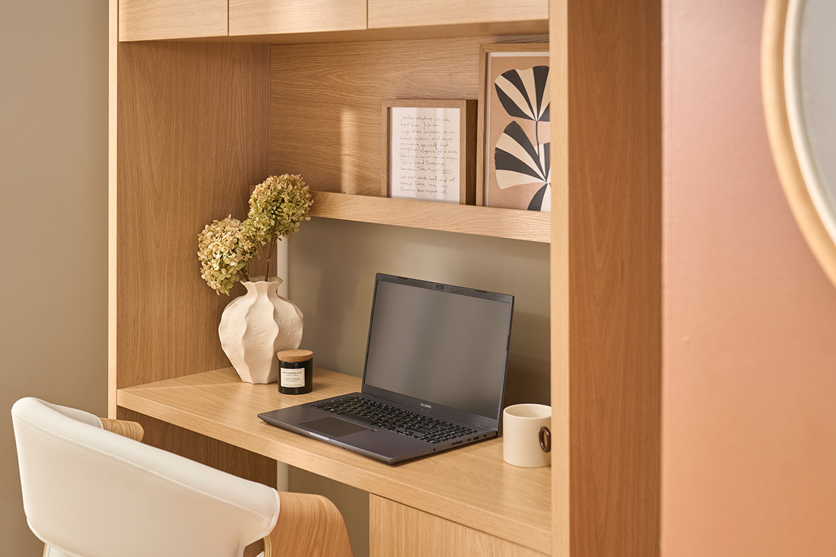 Bureau biblioth�que en bois clair avec rangements, d�cor� de vases, livres et ordinateur portable.