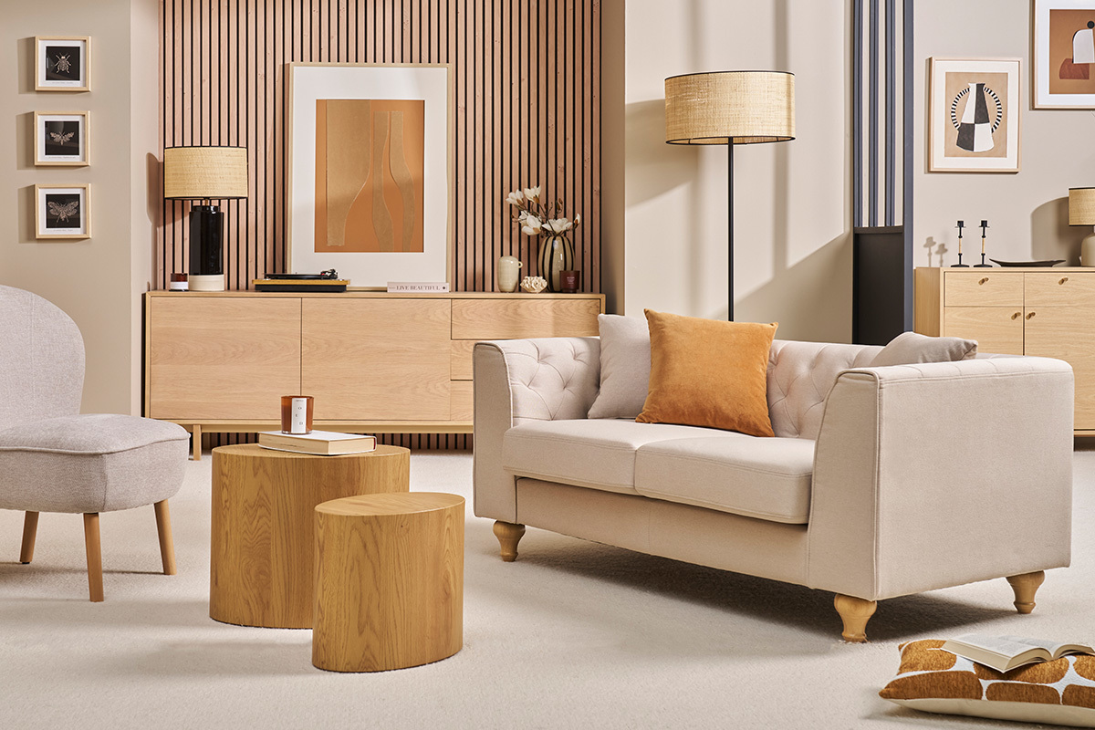 Canap 2 places capitonn beige MONTAIGNE en tissu, vue de ct avec coussin orange, dans un salon lgant.