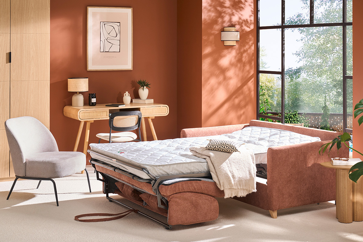 Canap convertible en tissu terre brle ouvert en lit avec matelas, table et chaise en fond.