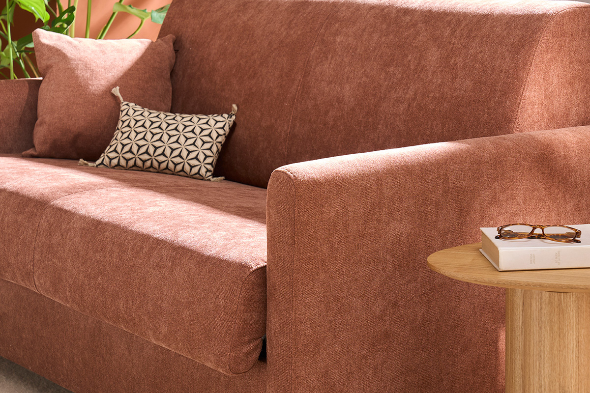 Canap convertible en velours terre brle, accoudoir droit et coussins avec petite table en bois.
