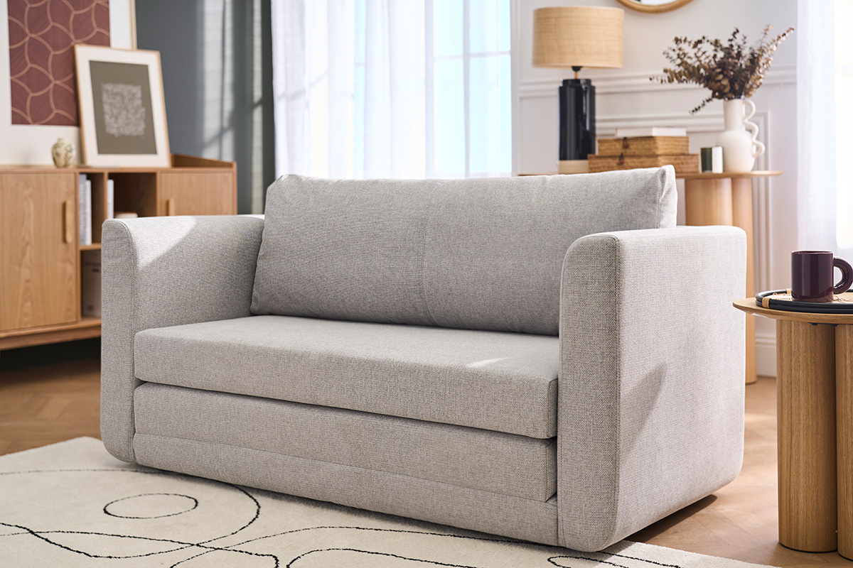 Canap� convertible 2 places en tissu gris clair, vue de face, dans un salon moderne.