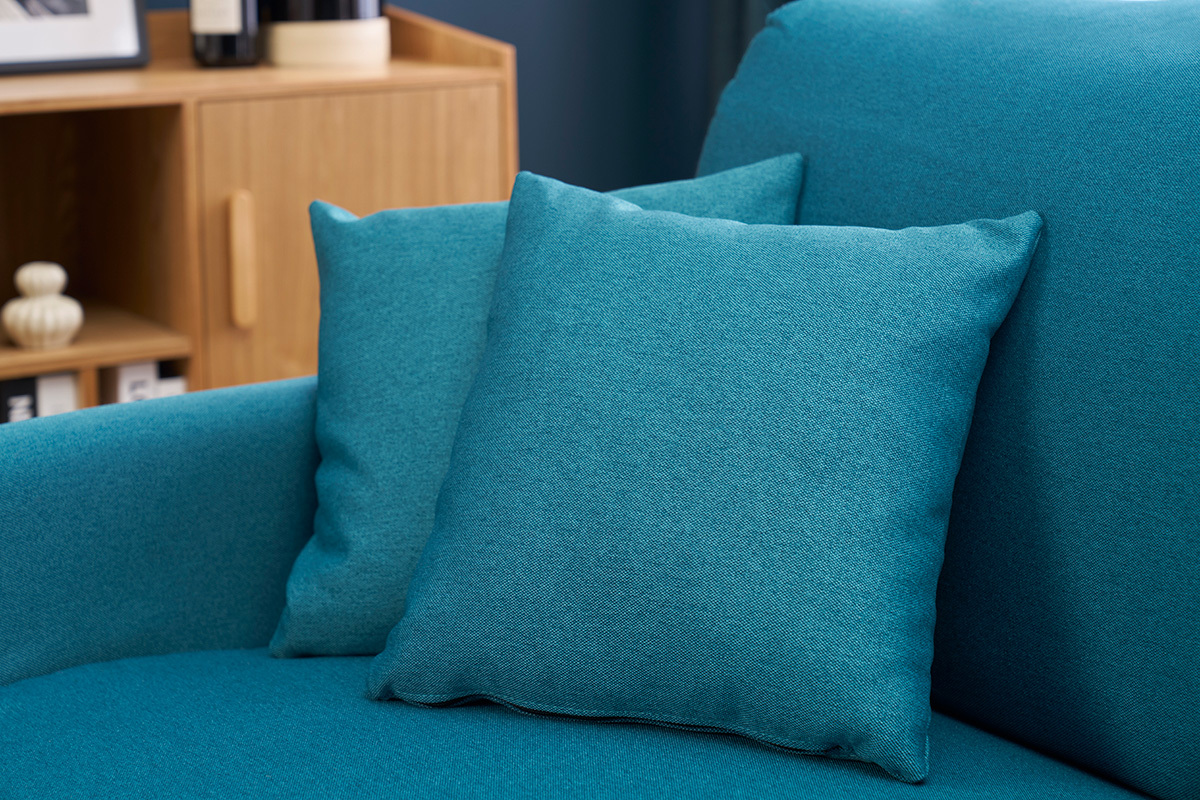 Coussins du canap convertible bleu canard SKANDY en vue rapproche  ct d'un meuble en bois.