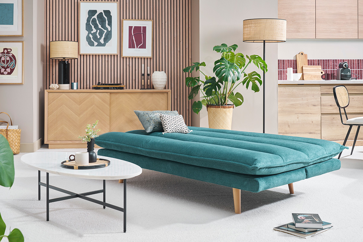Canap convertible bleu canard en position lit, pieds en bois clair, table basse et dcoration intrieure.