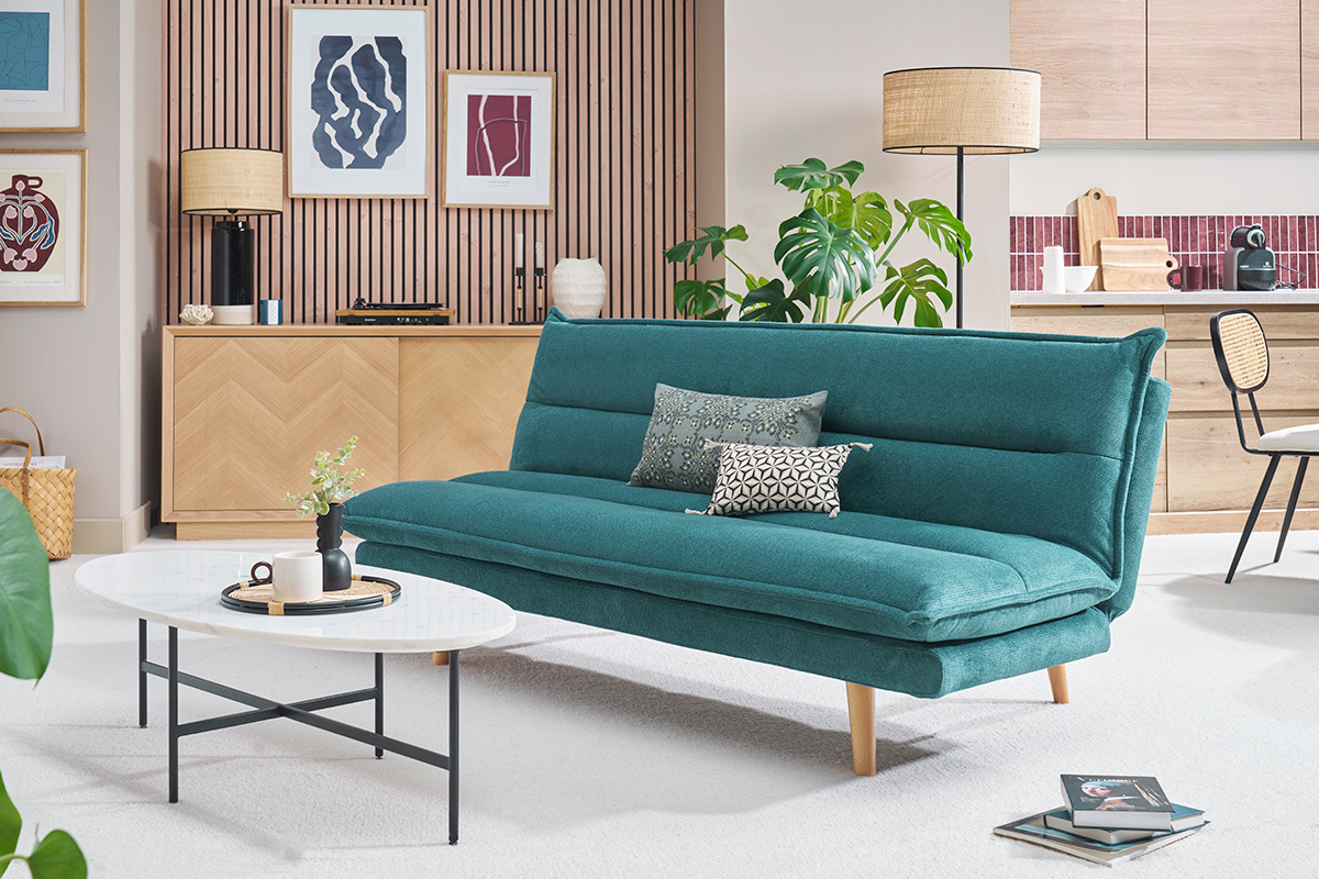 Canap convertible bleu canard avec pieds en bois clair devant une table basse blanche.
