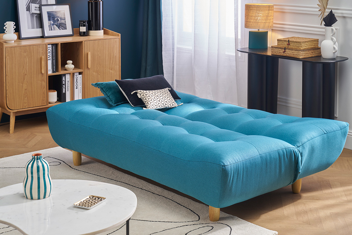 Canap convertible scandinave bleu canard avec pieds en bois, vu de ct dans un salon.