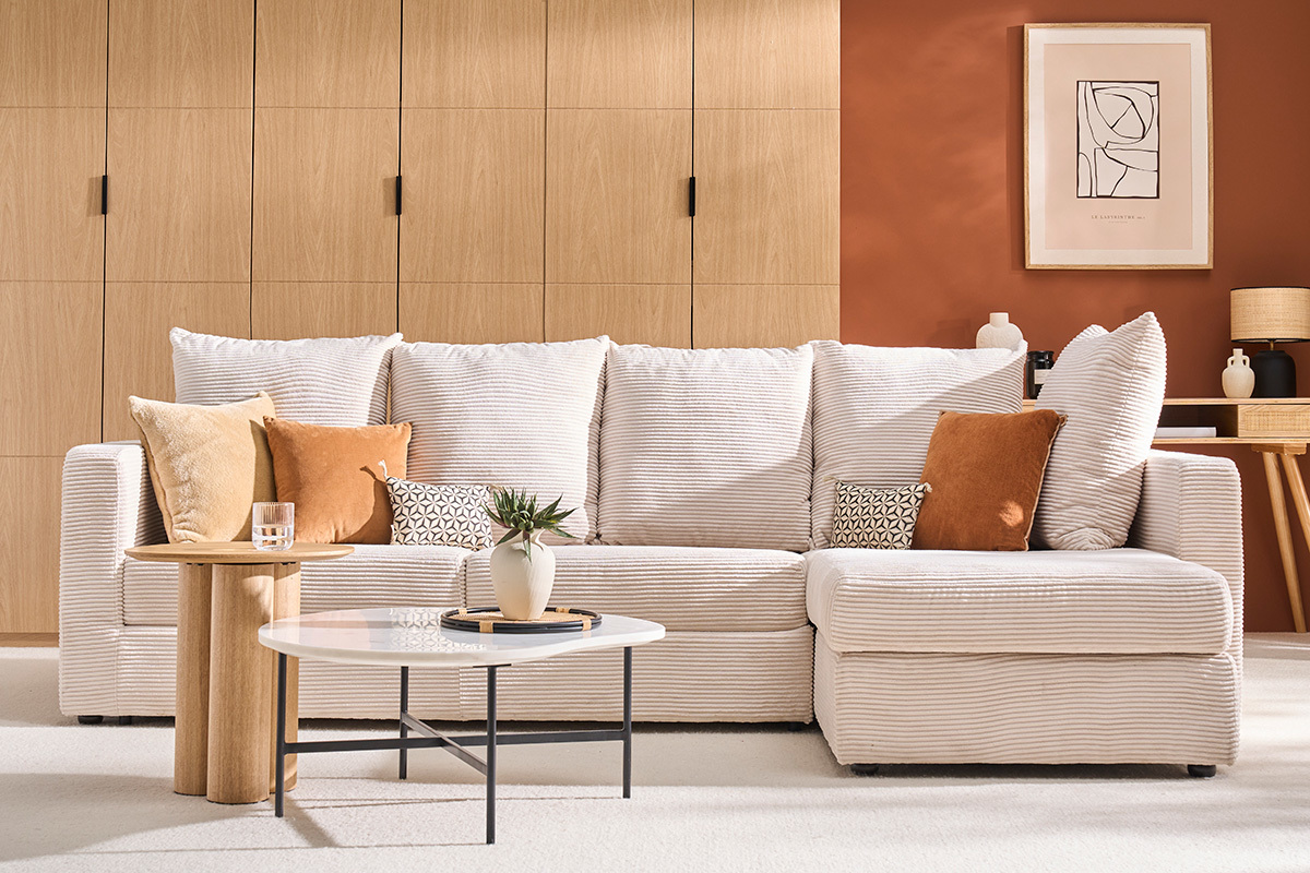 Canap d'angle convertible en velours ctel beige, coussins assortis, table basse et plante, fond bois clair.