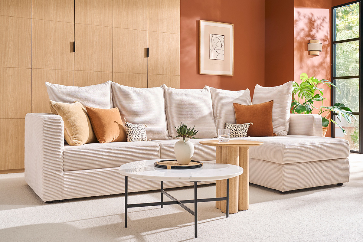 Canap d'angle convertible beige en velours ctel avec coussins, table basse en marbre, vue de ct.