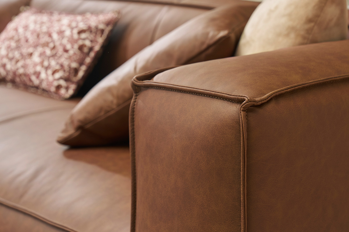 Accoudoir du canap d'angle en cuir marron avec coussins.