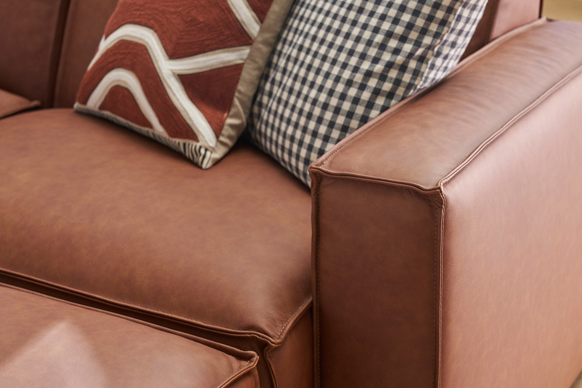 Gros plan sur un canap en cuir marron avec coussins  motifs.
