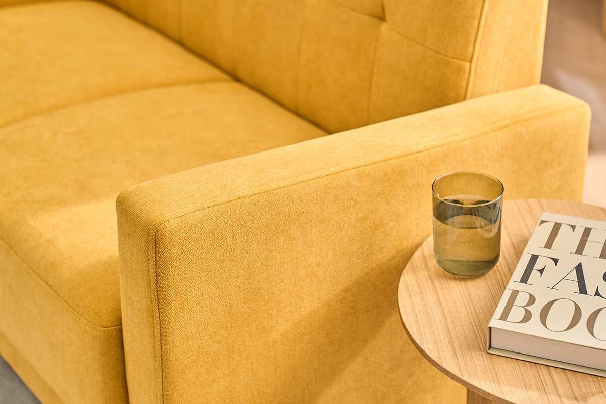 Canap� 2 places jaune moutarde effet velours, accoudoir en gros plan, table d'appoint avec verre et livre.