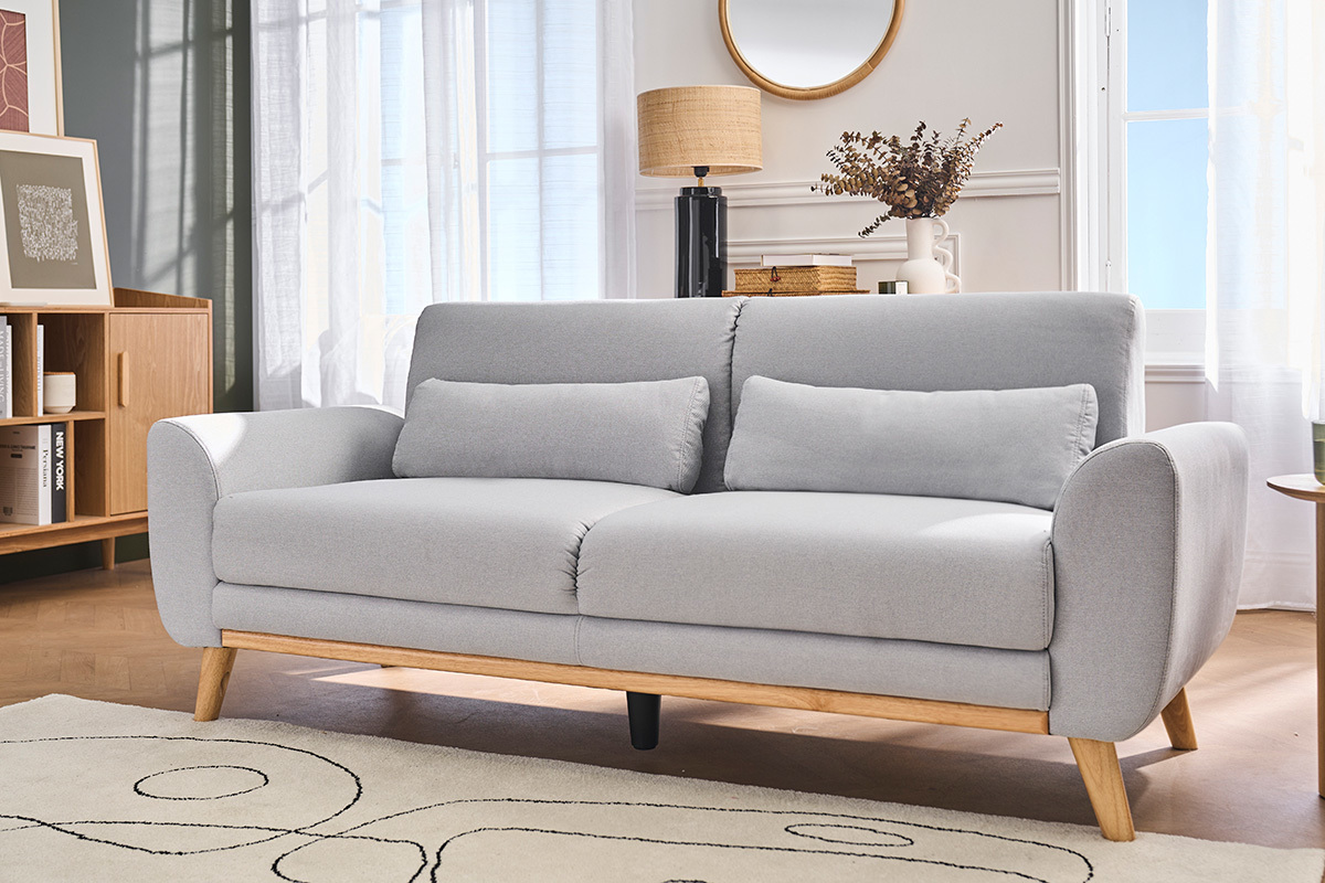 Canap� scandinave 3 places, tissu gris clair, pieds en bois clair, vue de 3/4dans un salon.