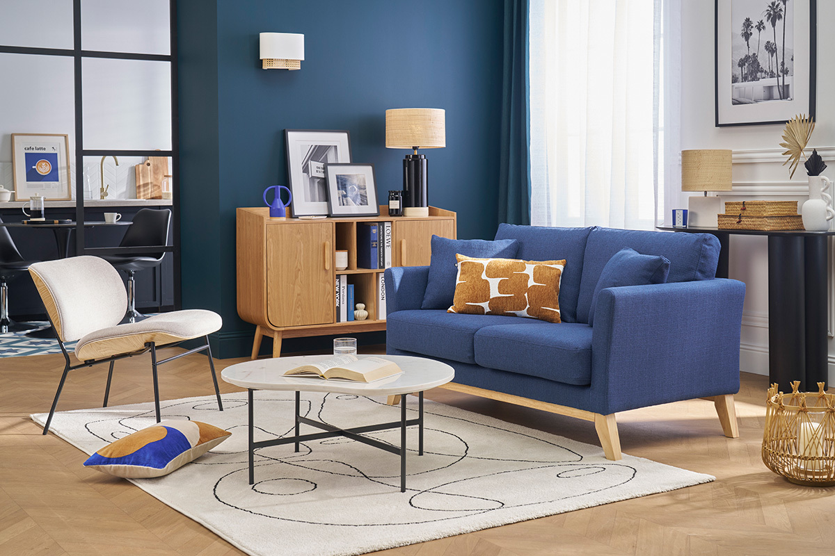 Salon avec canap scandinave bleu fonc en tissu et pieds en bois, table basse et meuble en bois clair.