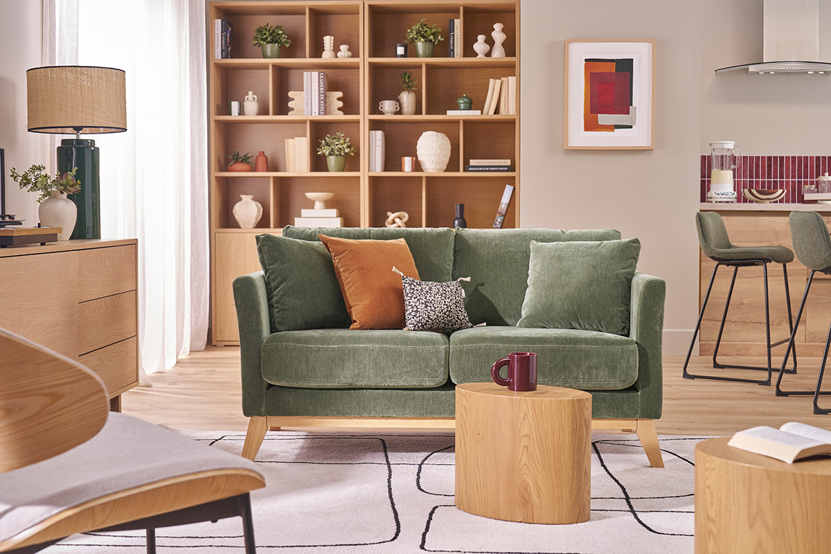 Canap� scandinave 2 places vert kaki Oslo, pied en bois, dans un salon avec table en bois et �tag�res.