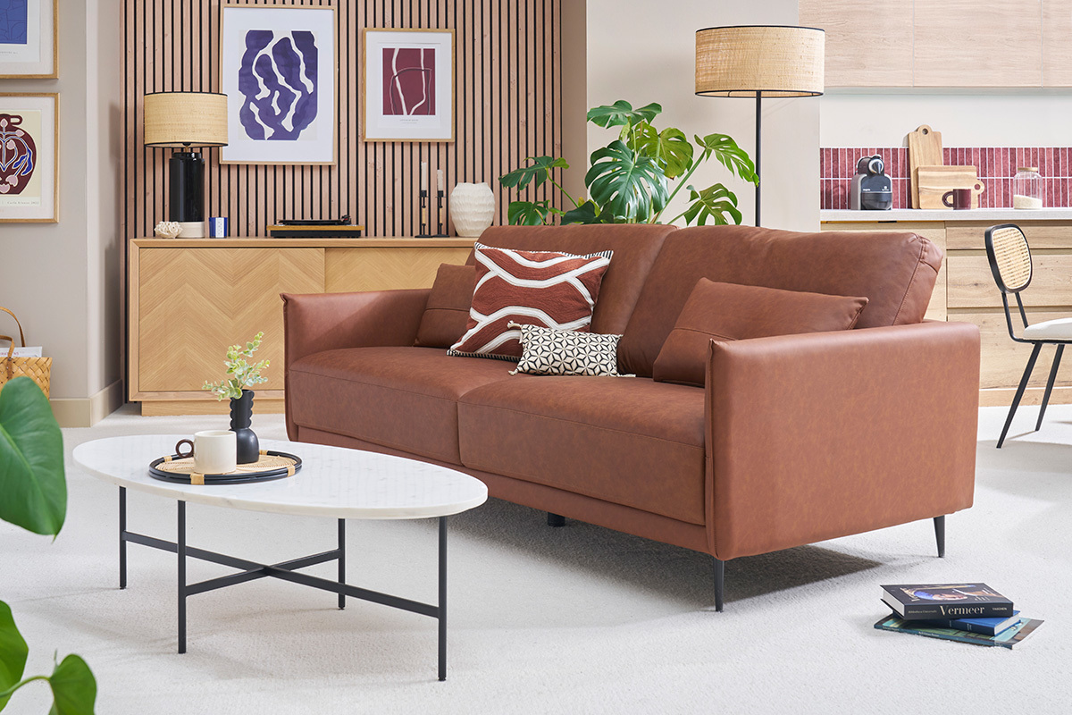 Canap vintage 3 places en cuir marron avec coussins, vue de 3/4, dans un salon.