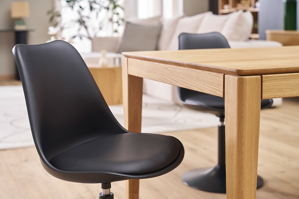 Chaise pivotante noire STEEVY V2 prs d'une table en bois, vue 3/4.