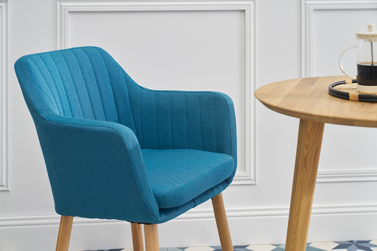Chaise scandinave bleue ALEYNA en tissu, vue de ct, avec une table en bois.