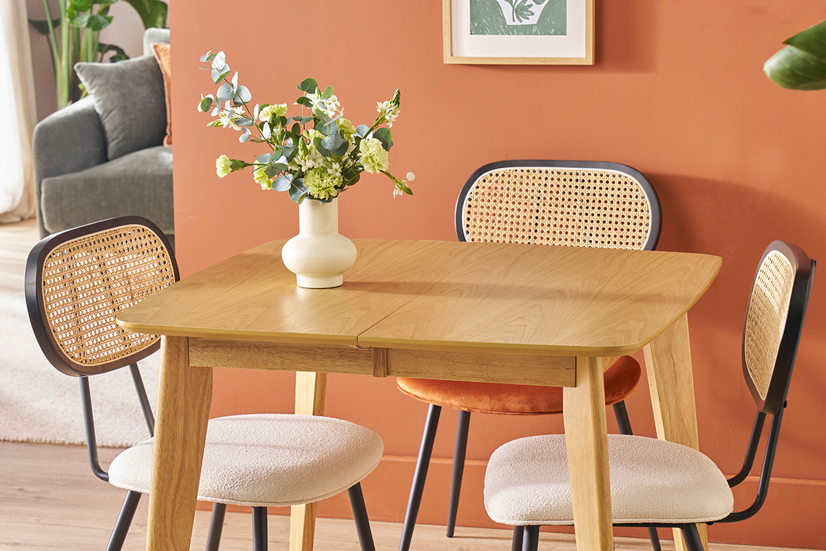 Deux chaises SWANN en tissu blanc et rotin autour d'une table en bois clair, vase avec fleurs.