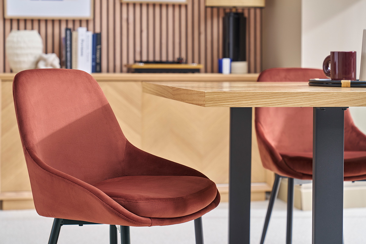 Deux chaises en velours rouge tomette et mtal noir entourant une table en bois.