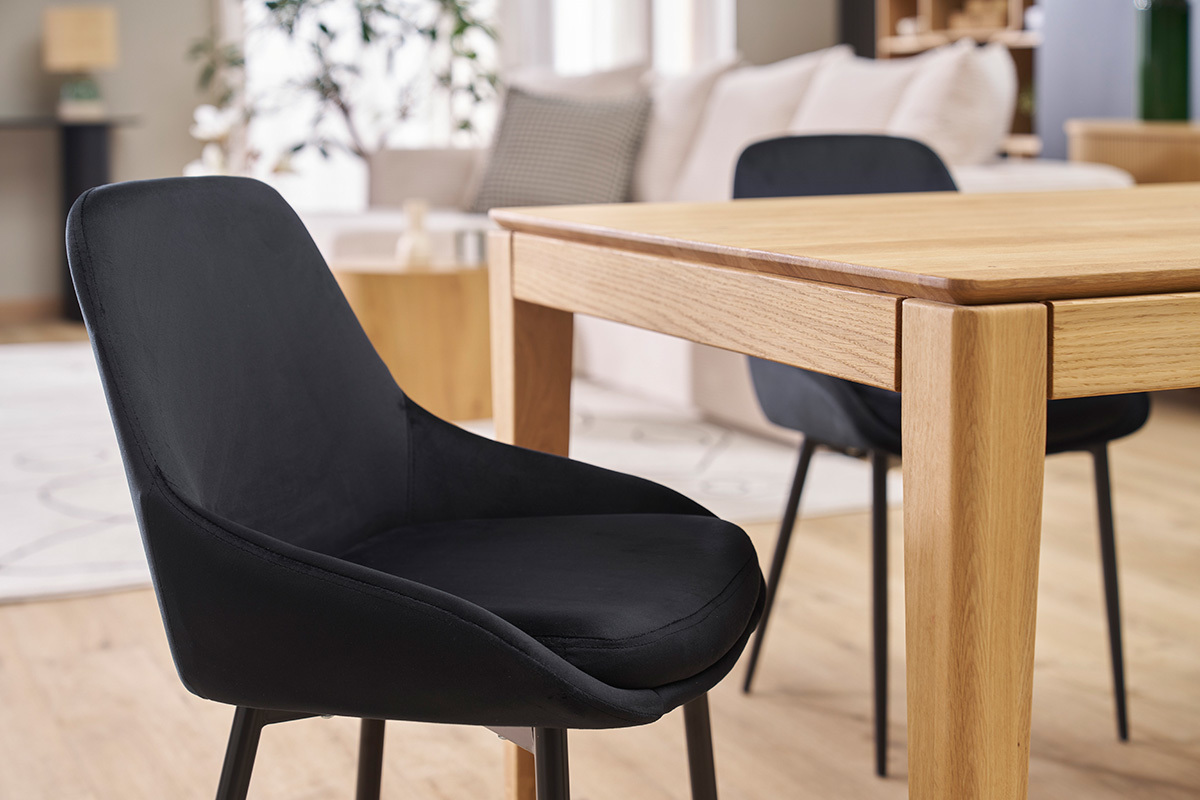 Chaise design noire en velours et mtal vue latrale proche d'une table en bois.