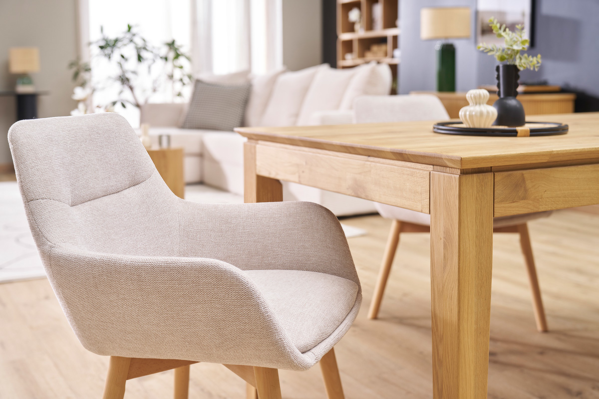 Chaise en tissu effet velours beige avec pieds en bois clair, vue prs d'une table en bois.