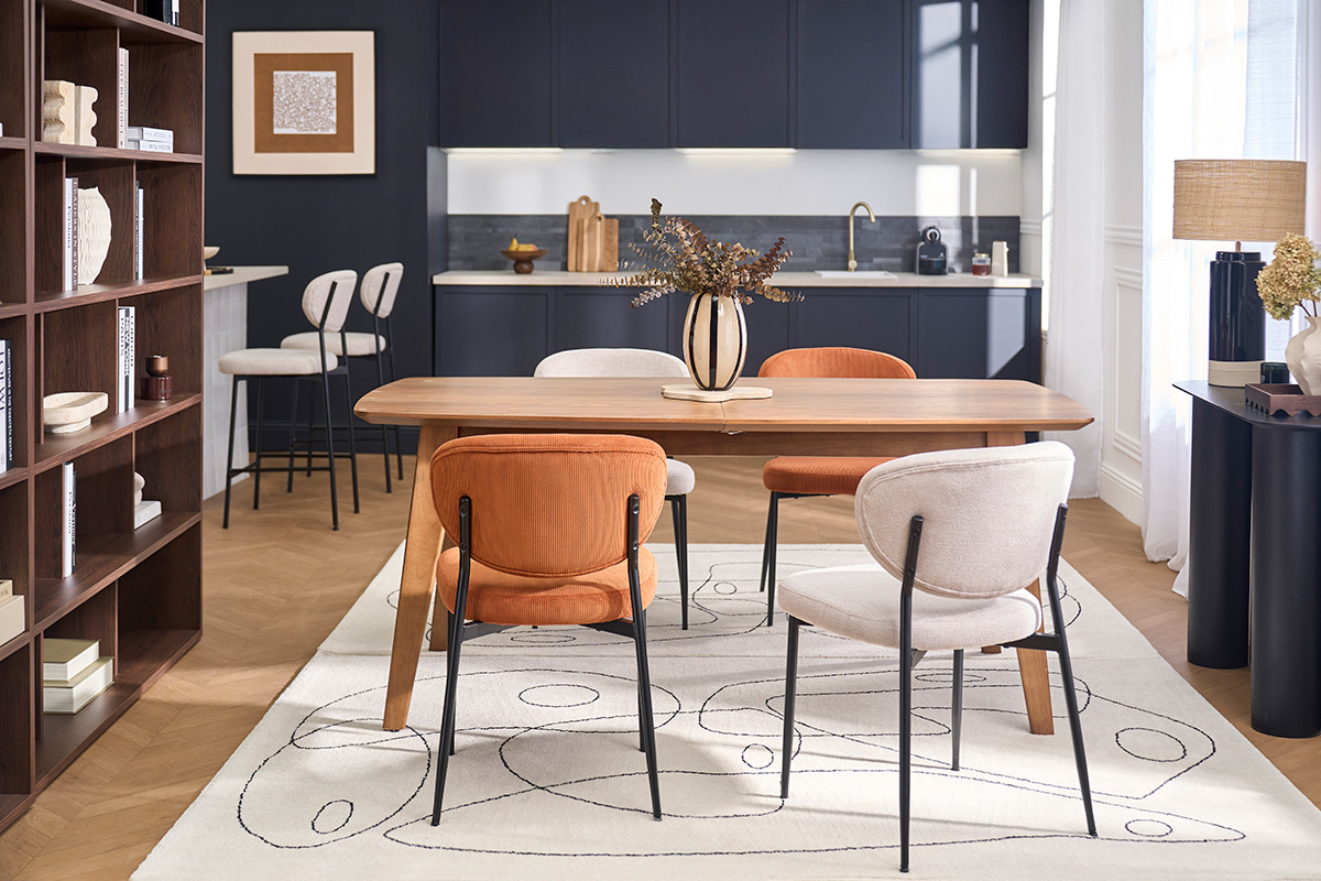 Salle � manger avec chaises en tissu beige et orange autour d'une table en bois, cuisine en arri�re-plan.