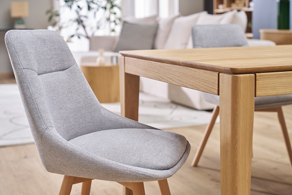 Chaise en tissu effet velours gris clair avec pieds en bois clair, vue de profil prs d'une table.