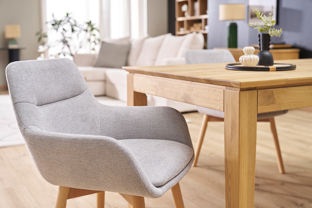 Chaise en tissu gris clair et bois clair, vue de ct,  ct d'une table en bois.