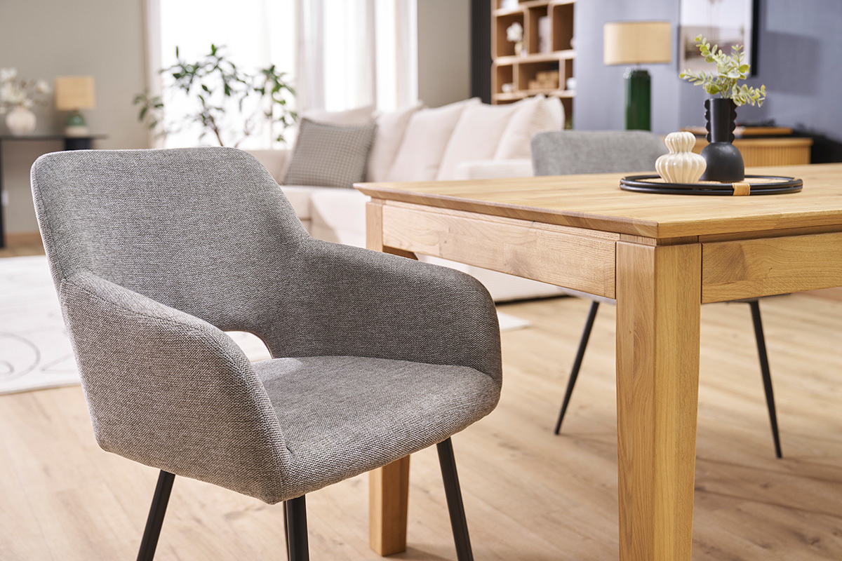 Chaise en tissu effet velours gris avec pieds en mtal noir, vue 3/4 prs d'une table en bois.