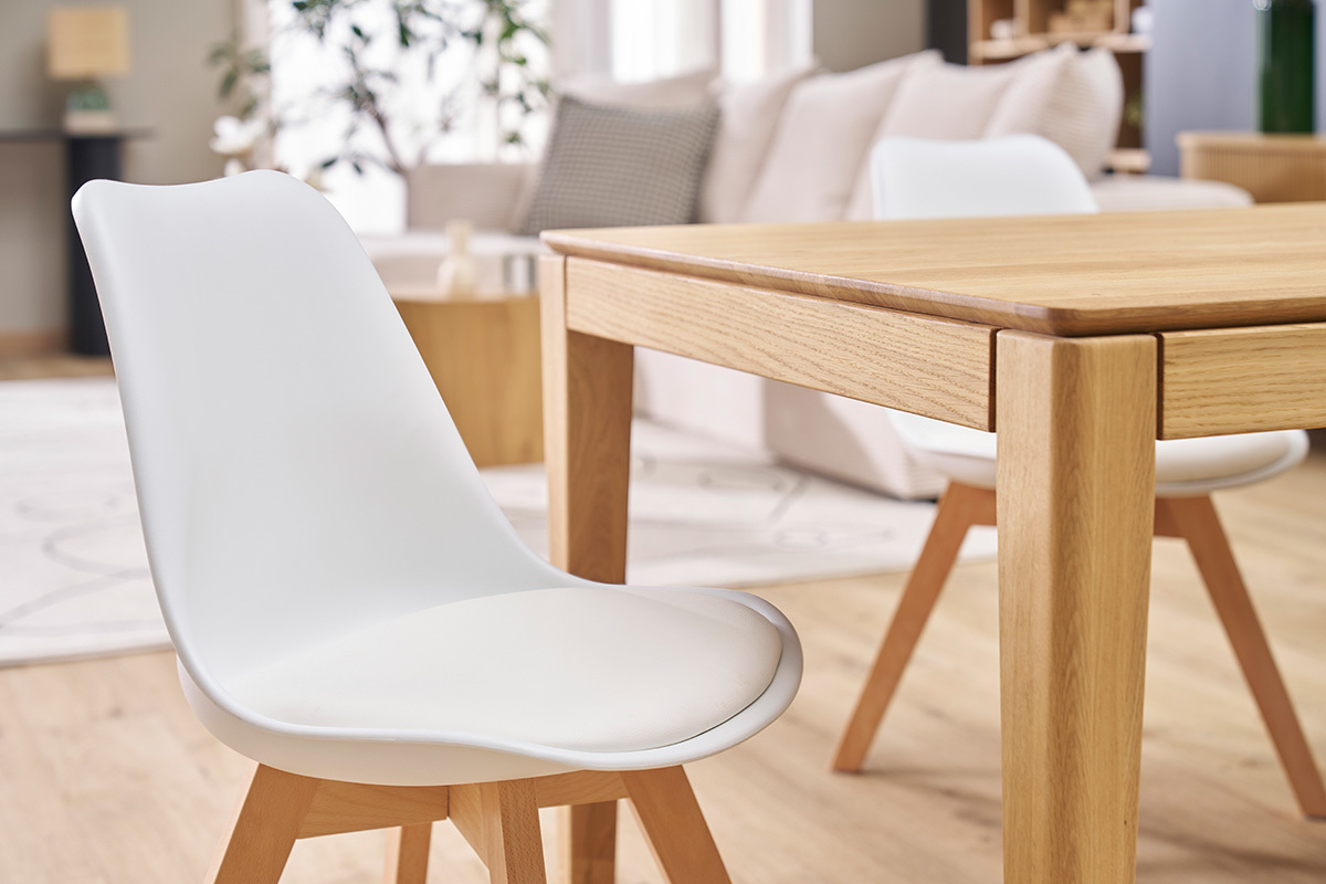 Chaises scandinaves blanches et table en bois clair dans un salon lumineux.