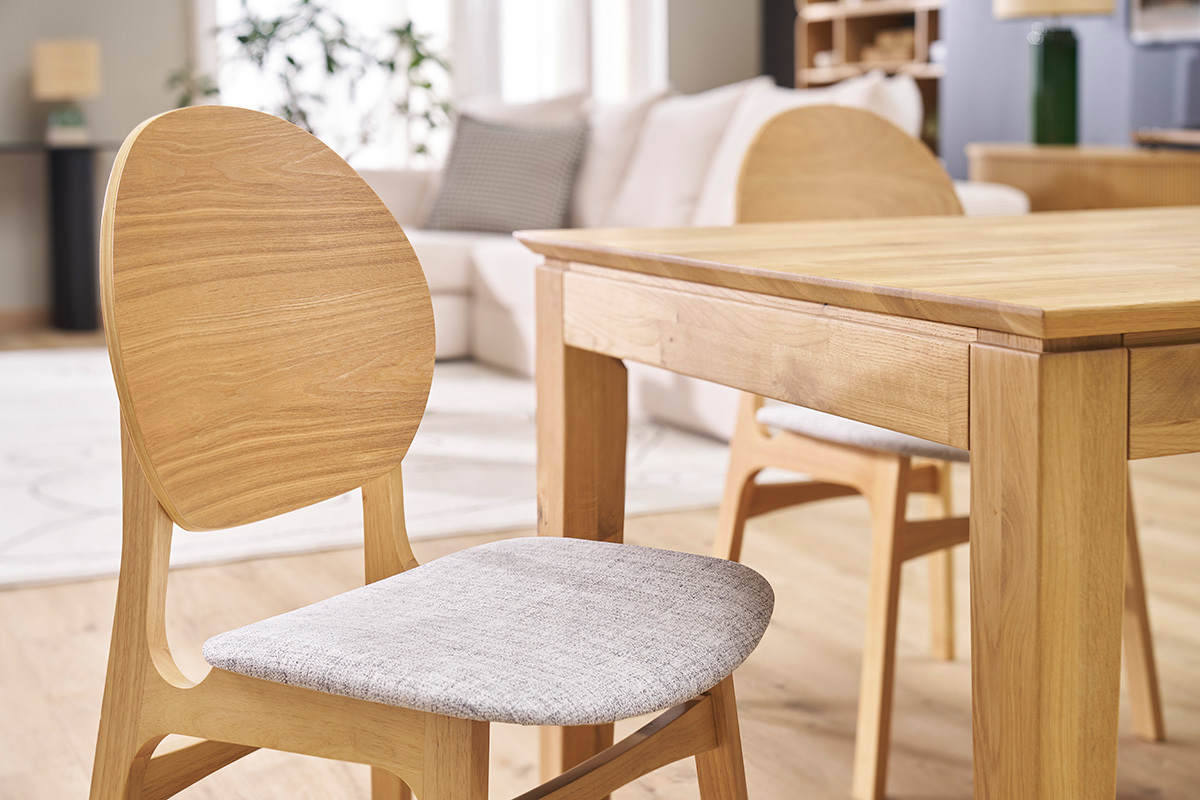 Chaises scandinaves en bois clair et tissu gris devant une table en bois, vue de ct.