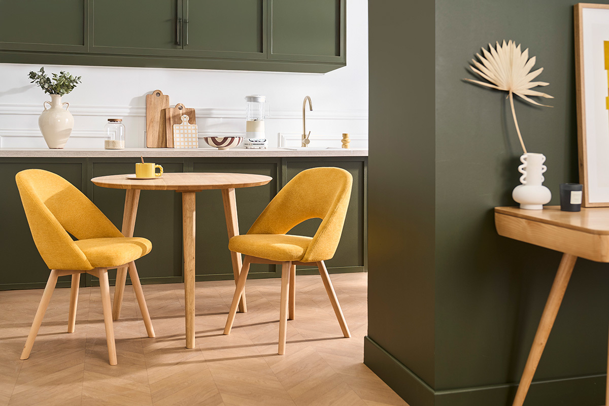 Deux chaises scandinaves en tissu jaune moutarde et bois clair autour d'une table ronde en bois.