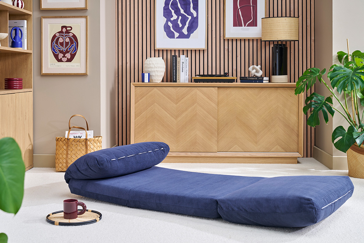 Chauffeuse en velours ctel bleu fonc SPENCER dplie sur tapis, avec meuble en bois et plantes en arrire-plan.