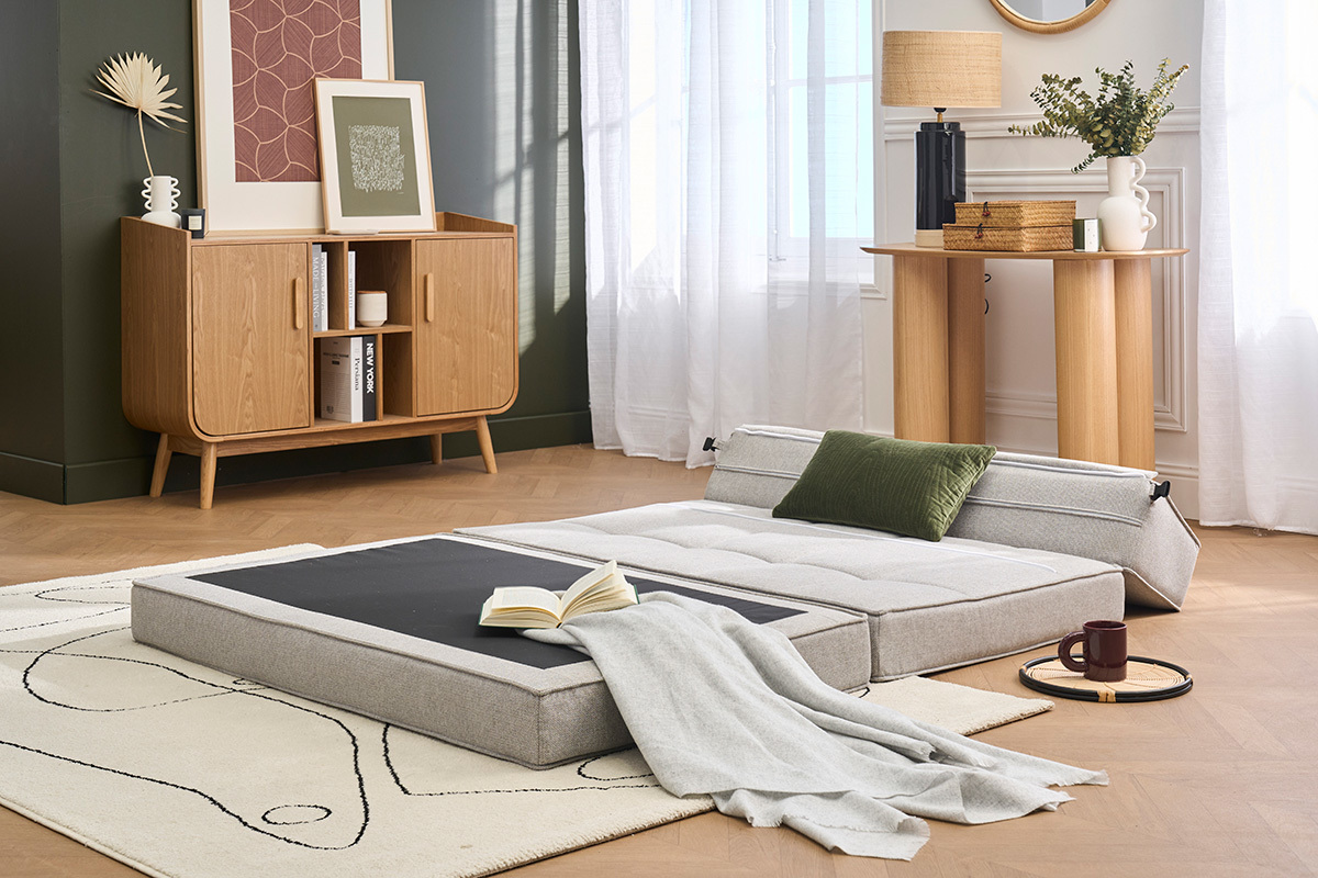 Chauffeuse 2 places KATY d�pli�e en lit, tissu gris clair, coussin vert, situ�e dans un salon moderne.