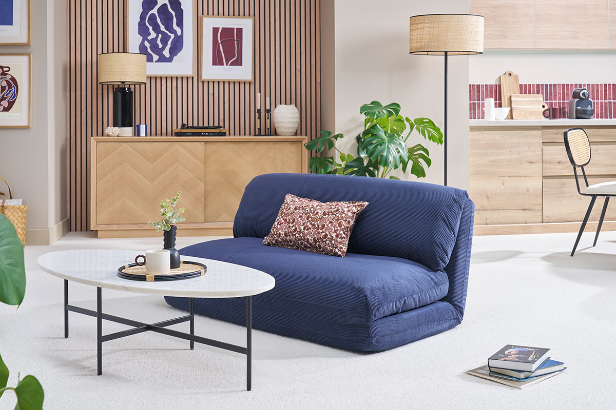 Chauffeuse convertible en velours ctel bleu fonc, vue de face dans un salon moderne.