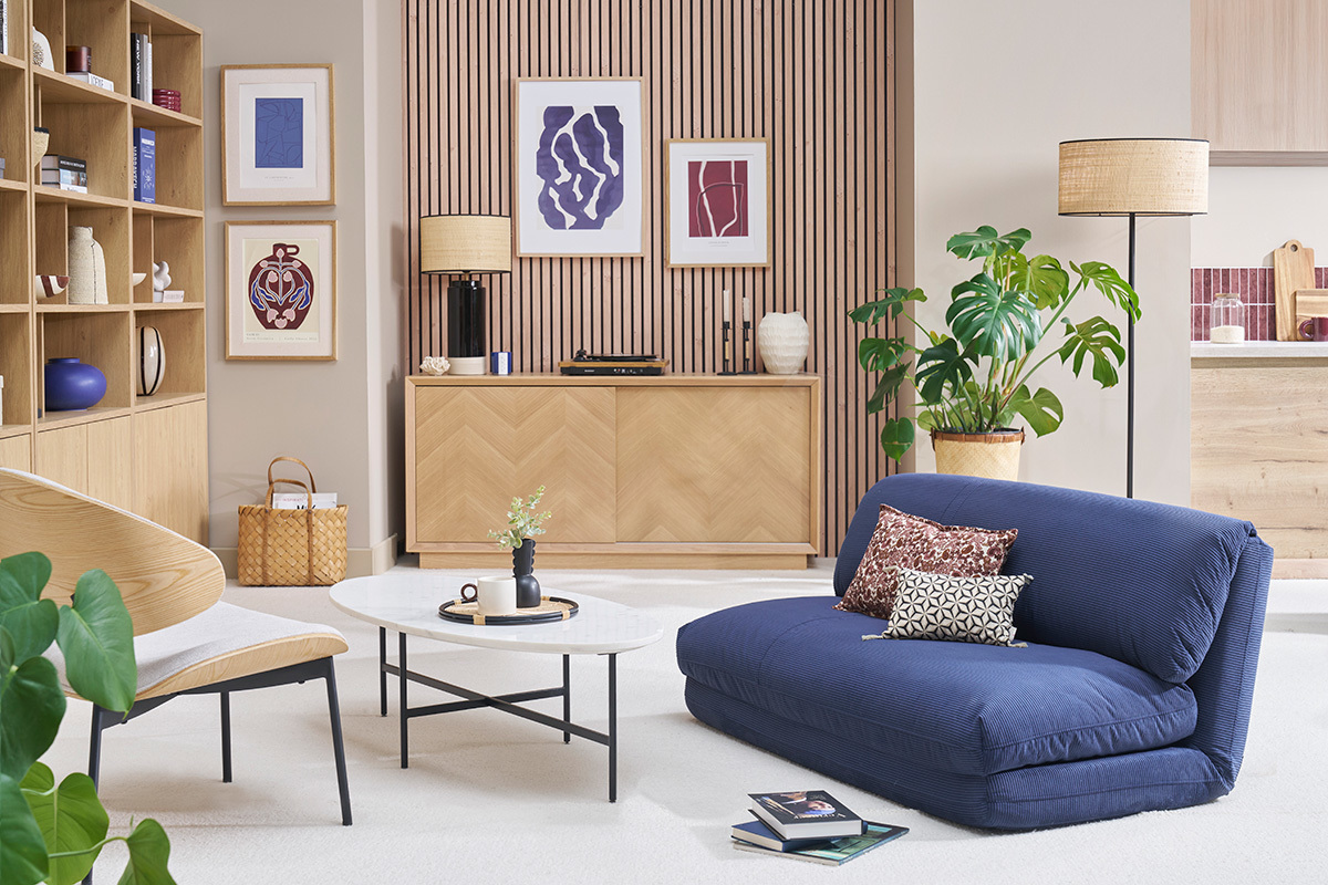 Chauffeuse convertible bleu fonc dans un salon avec table basse et tagre en bois.