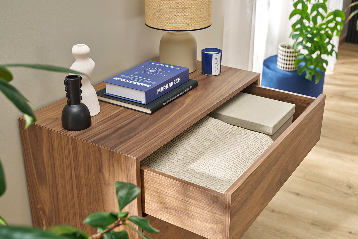 Commode en bois fonc avec tiroir ouvert, lampes et livres sur le dessus.