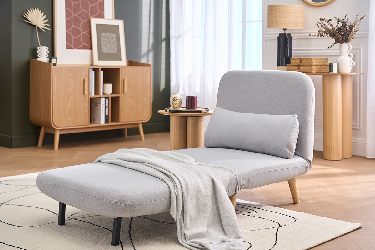 Fauteuil convertible AMIKO gris clair en tissu, vue 3/4, avec plaid, table d'appoint et d�cor scandinave.