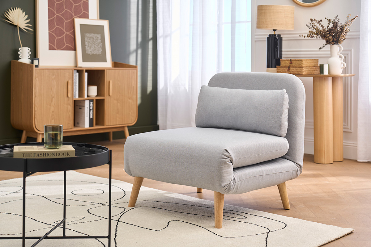 Fauteuil convertible en tissu gris clair et bois clair, vue de 3/4 dans un salon �l�gant.
