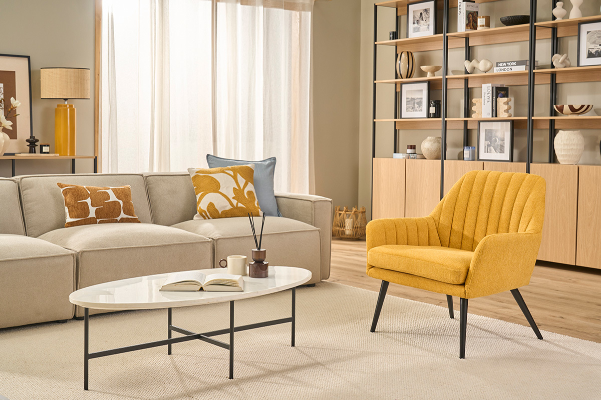 Fauteuil design GASTON en tissu jaune moutarde, vu de face, avec table basse et canap� dans un salon.