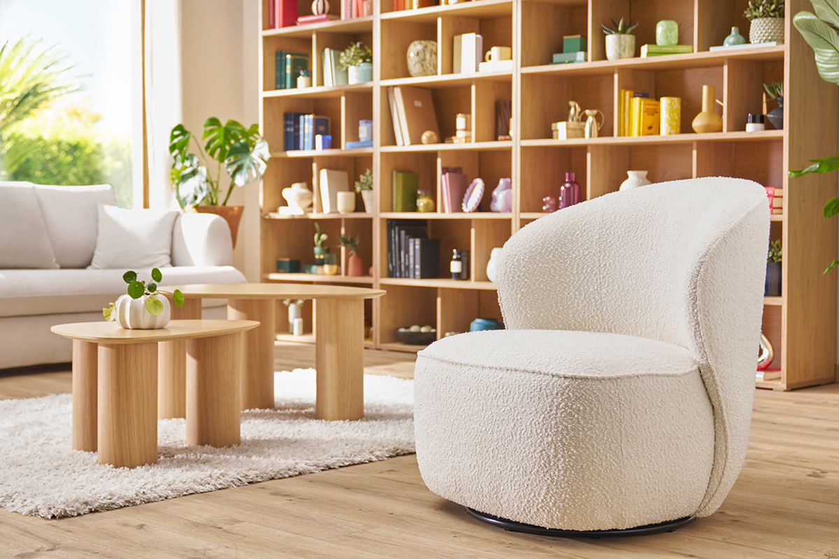 Fauteuil design pivotant blanc, vue de 3/4, avec des tables basses en bois et une biblioth�que en arri�re-plan.