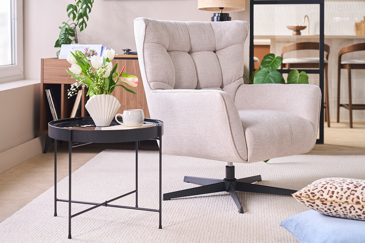 Fauteuil pivotant AVERY en tissu beige, angle 3/4, avec table et fleurs en arri�re-plan.