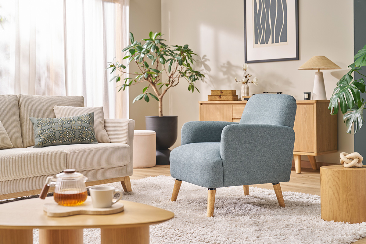Fauteuil scandinave en tissu avec pieds en bois clair, plac� dans un salon moderne.