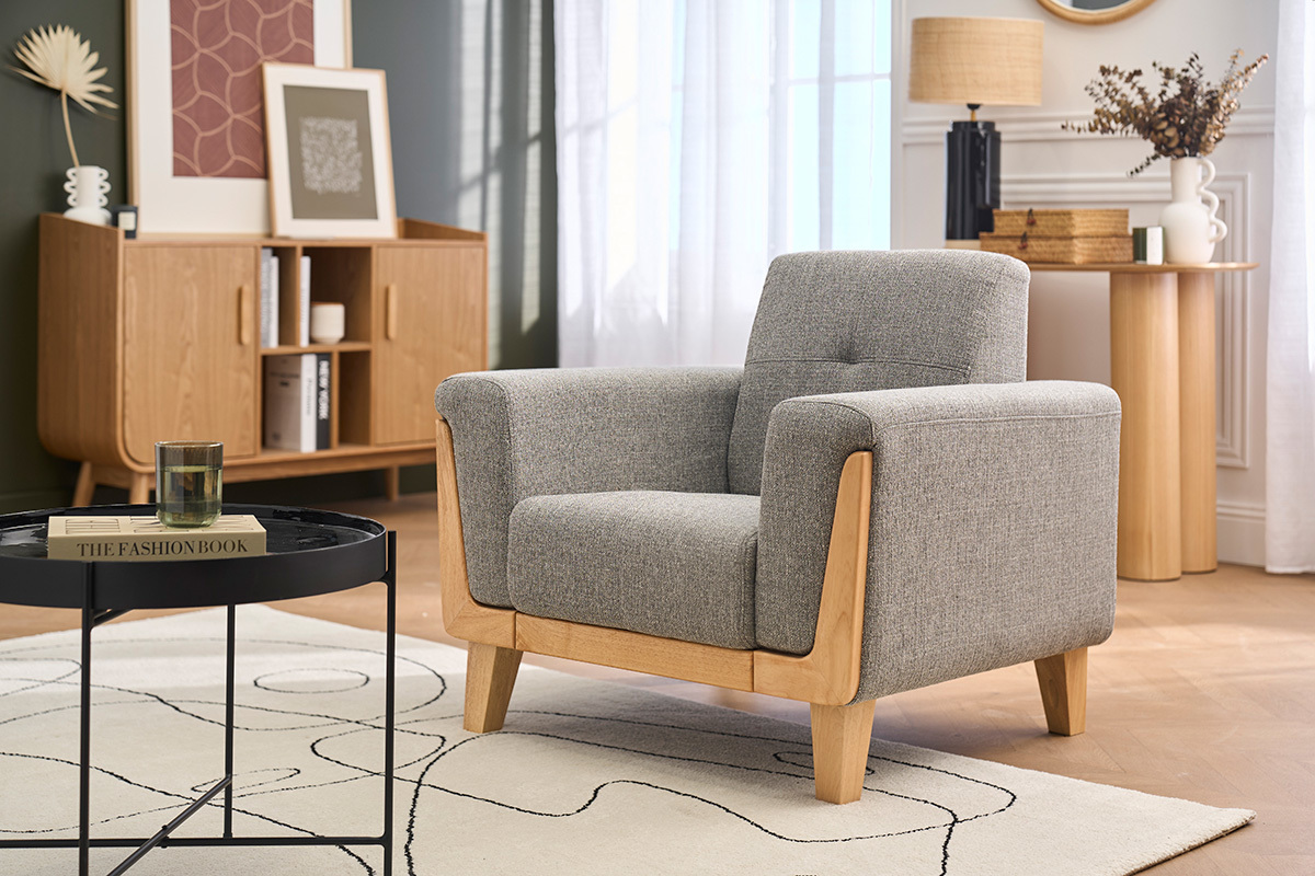 Fauteuil scandinave en tissu gris et bois clair, vue de 3/4, avec table basse et buffet en arri�re-plan.