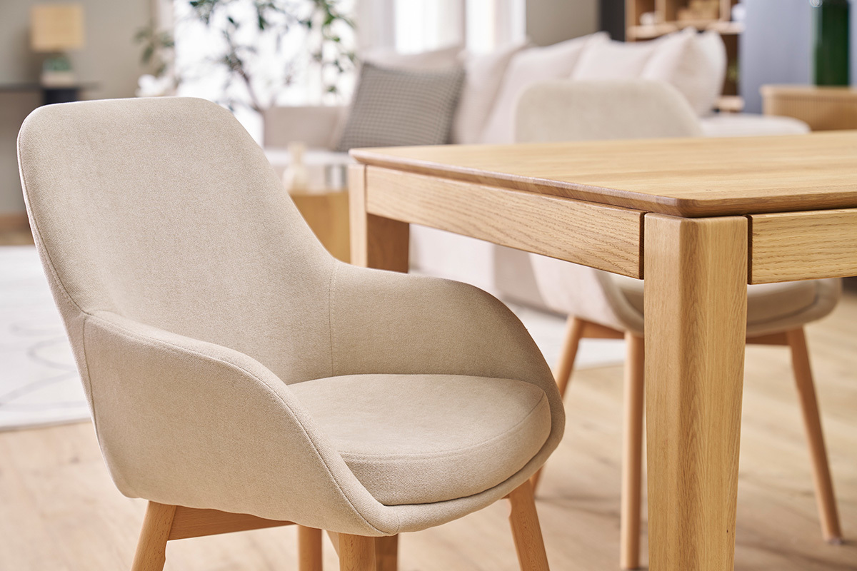 Fauteuil scandinave en tissu beige et bois clair, vue de profil,  ct d'une table en bois.