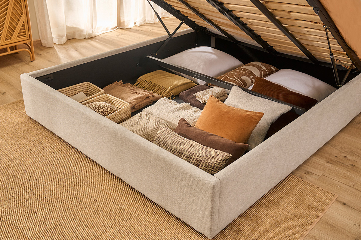 Lit coffre en tissu beige ouvert, avec rangement pour coussins et couvertures.