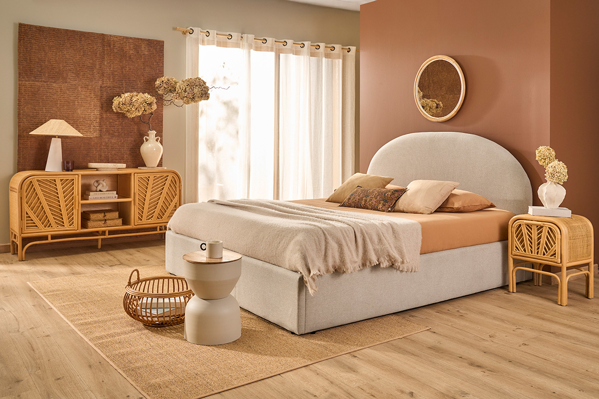 Lit coffre beige en tissu, deux places, avec mobilier en bois dans une chambre lumineuse.