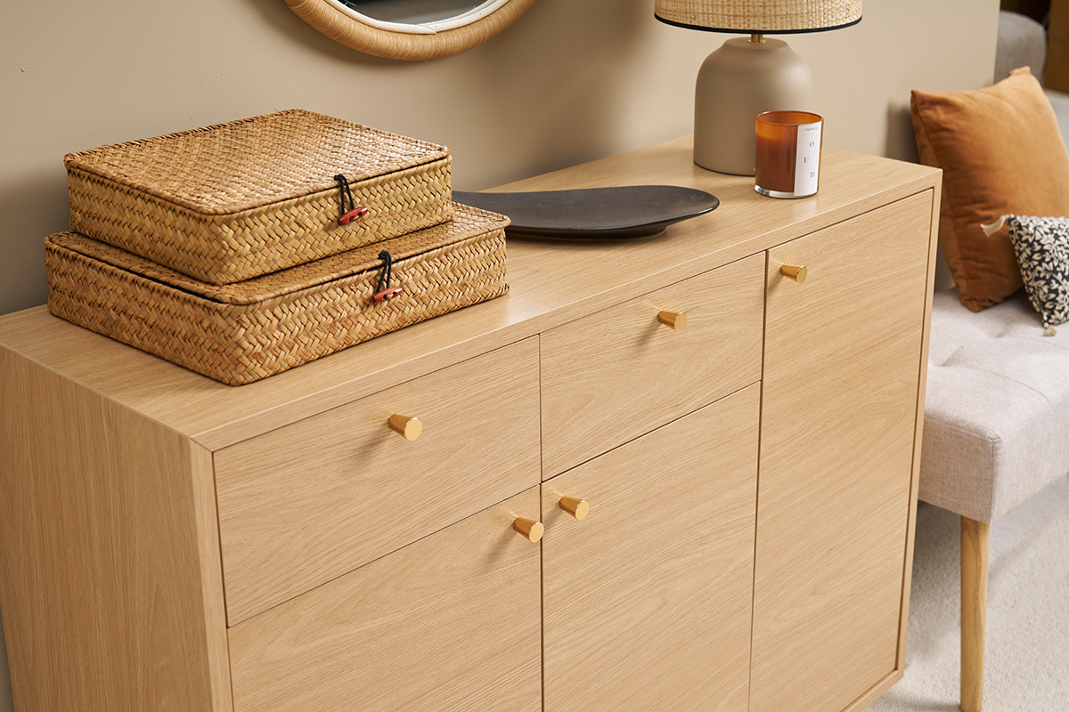 Meuble d'entre en bois clair avec poignes dores, deux paniers en osier et dcorations sur le dessus.