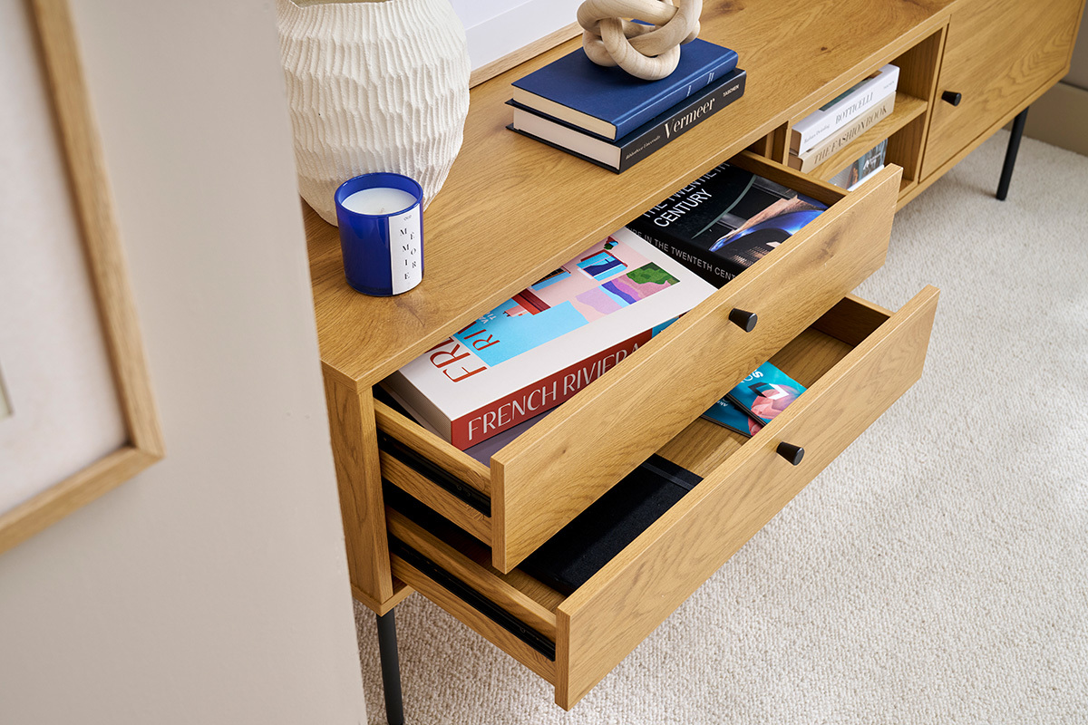 Meuble TV en bois clair avec tiroirs ouverts, livres et objets dco sur le dessus.