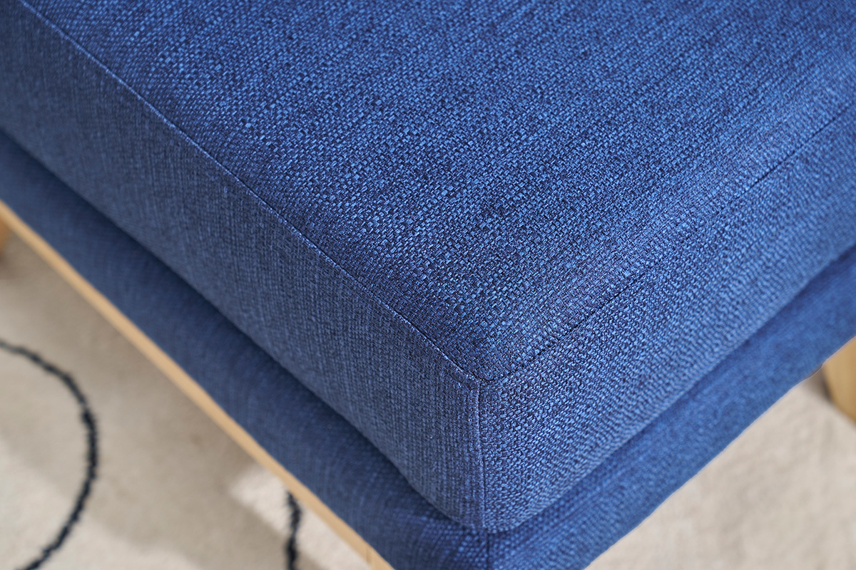 Gros plan sur le tissu bleu fonc d'un pouf repose-pieds scandinave.